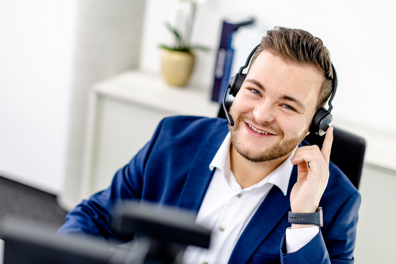 ein lächelnder Mann, der ein Headset und einen blauen Blazer trägt.