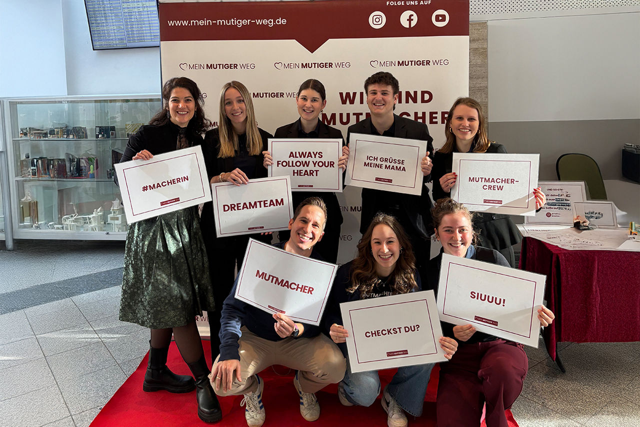 Acht Personen stehen vor der Leinwand und halten Karten mit lustigen Sprüchen in der Hand.