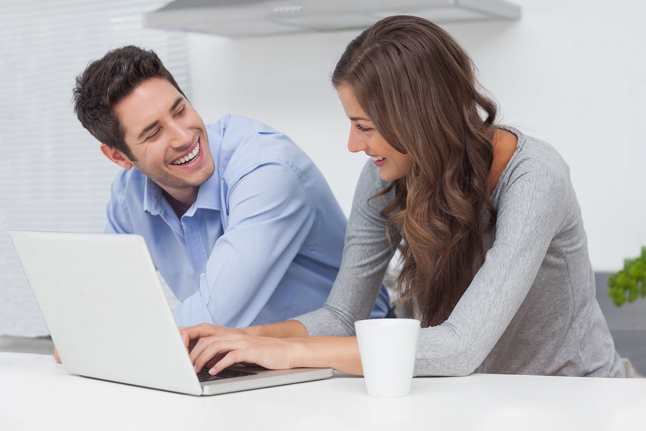 Ein Mann und eine Frau arbeiten gemeinsam am Laptop, lächeln sich an und wirken entspannt und konzentriert.