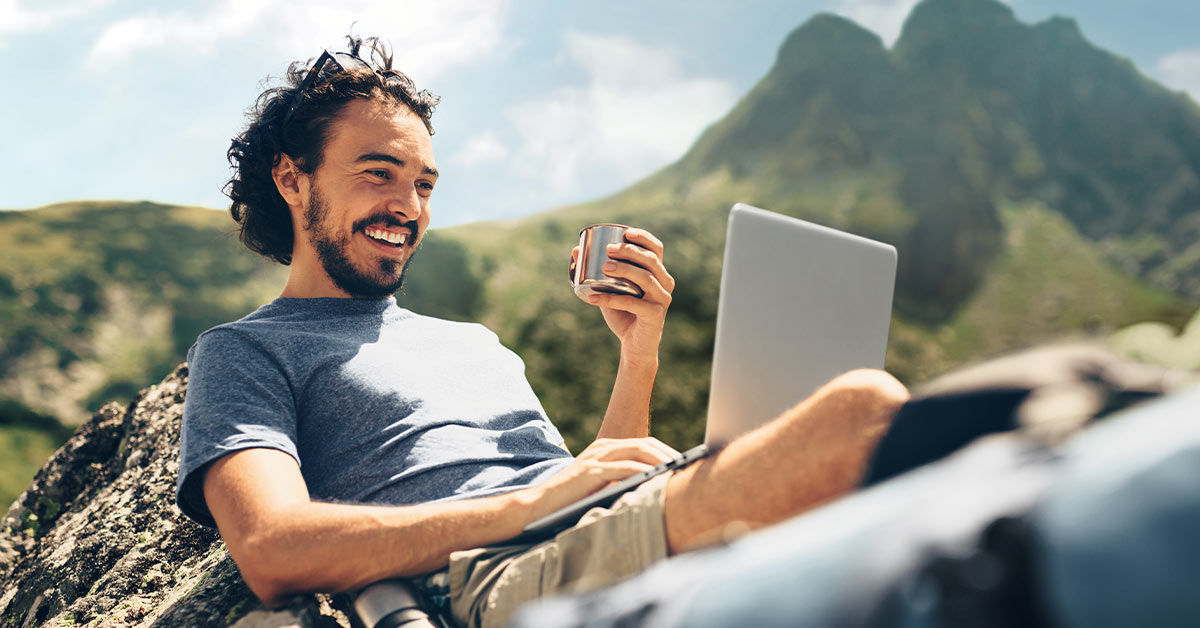 Mann sitzt in den Bergen am Laptop und macht OnlineBanking