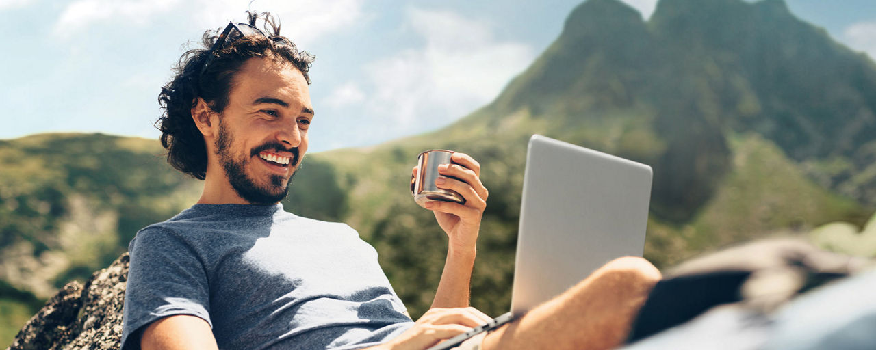 Mann sitzt im Gebirge am Laptop