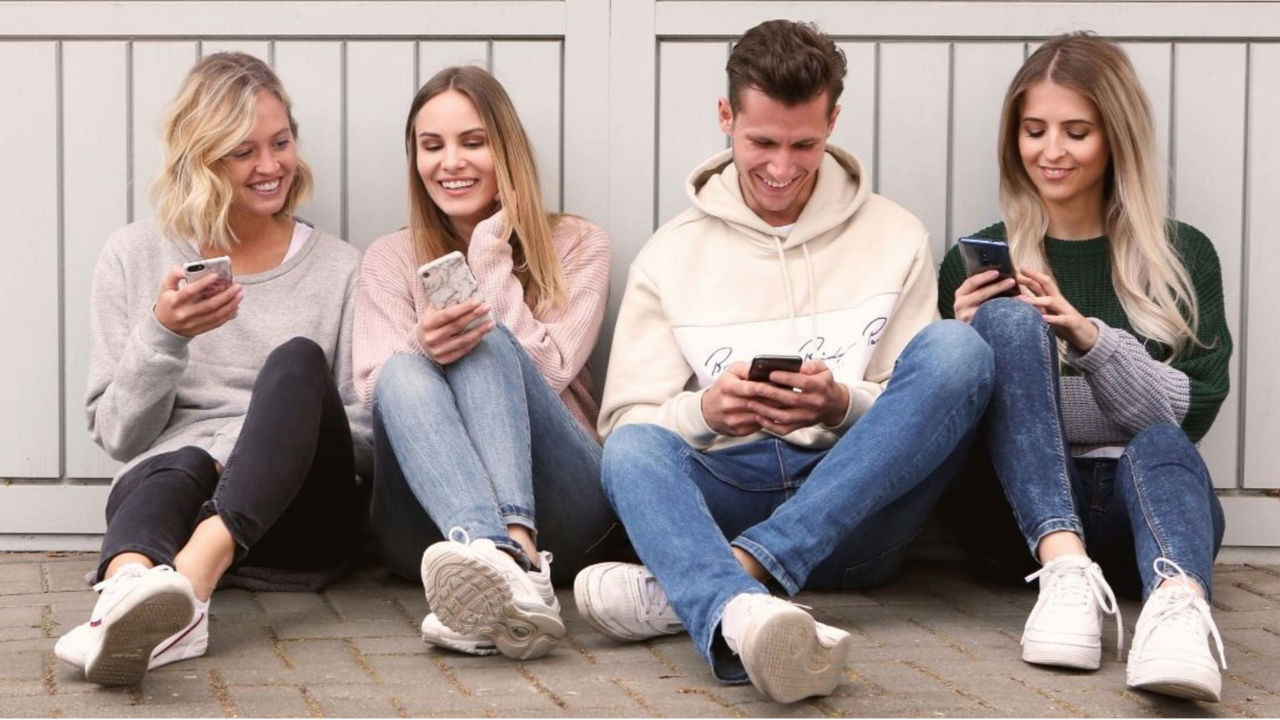Vier junge Menschen sitzen auf dem Boden und halten ein Smartphone in der Hand