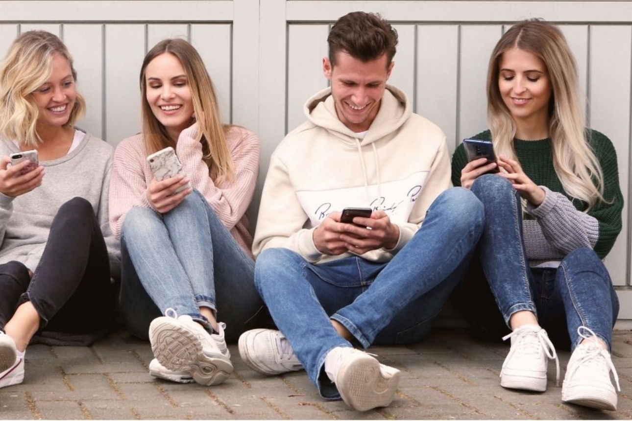 Vier junge Menschen sitzen auf dem Boden und halten ein Smartphone in der Hand