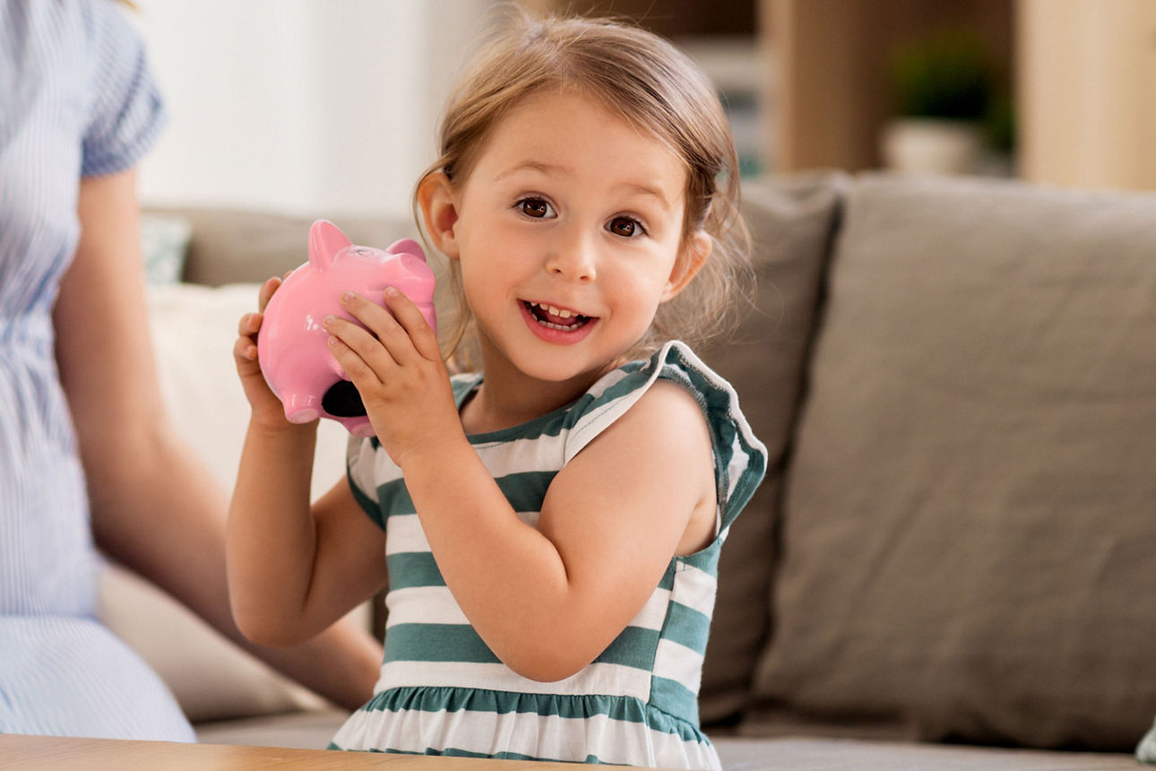 Kleines Mädchen hält lächelnd ein rosa Sparschwein in den Händen.