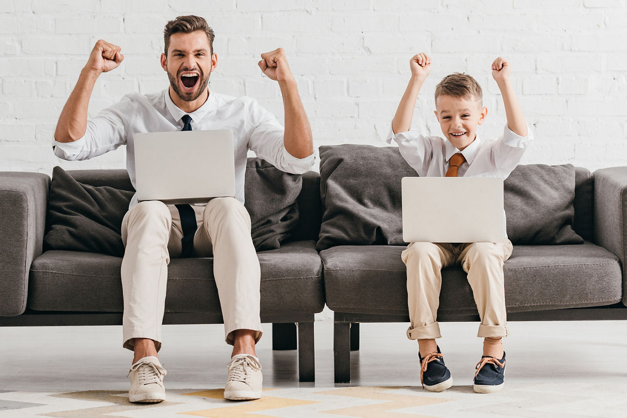 Vater und Sohn mit Laptop jubelnd auf einem Sofa