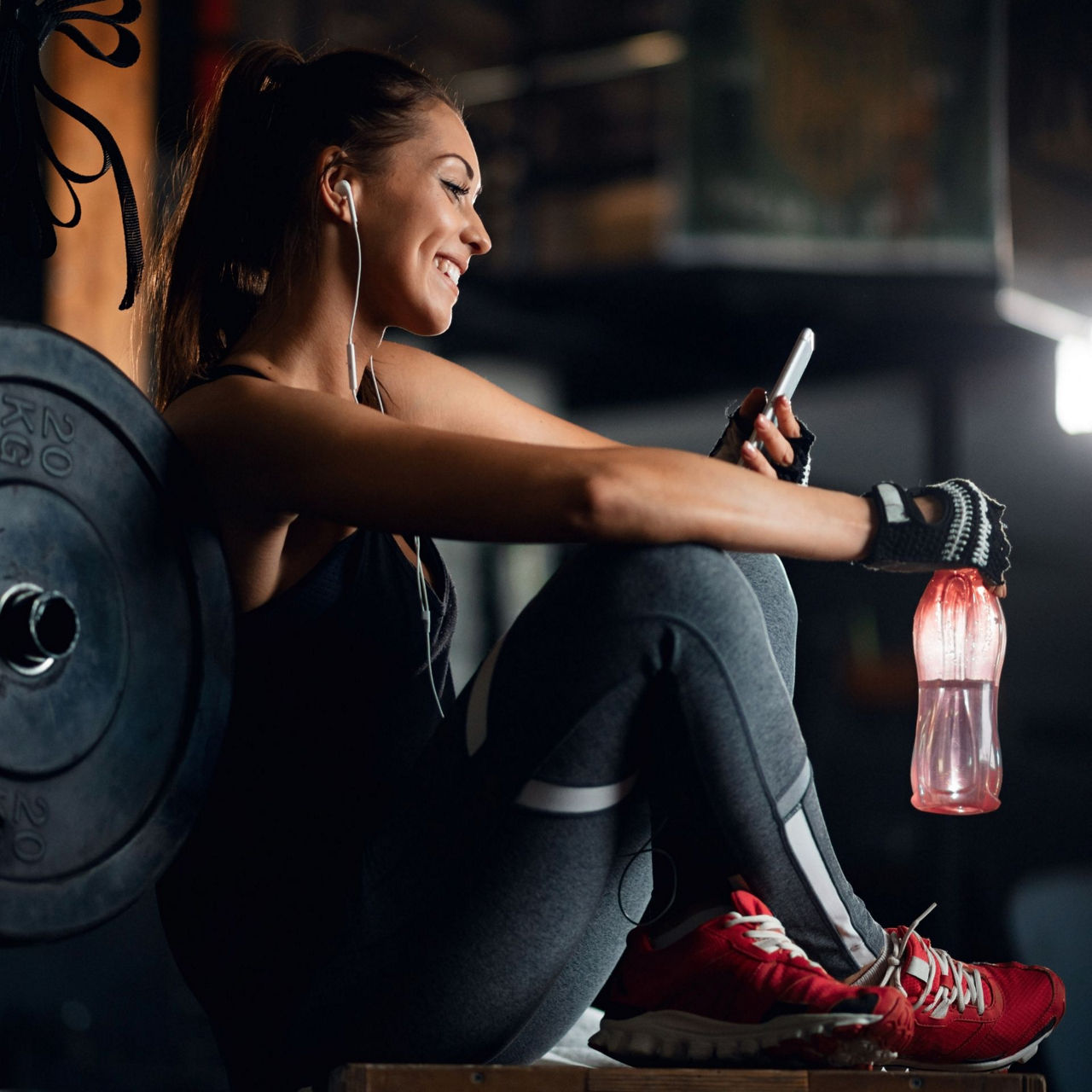 Junge Frau sitzt im Fitnessstudio und schaut auf ihr Handy