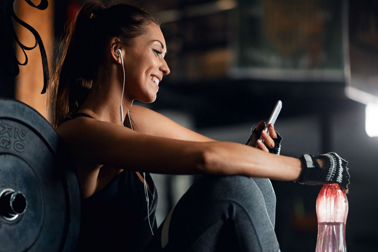 Junge Frau sitzt im Fitnessstudio und schaut auf ihr Handy
