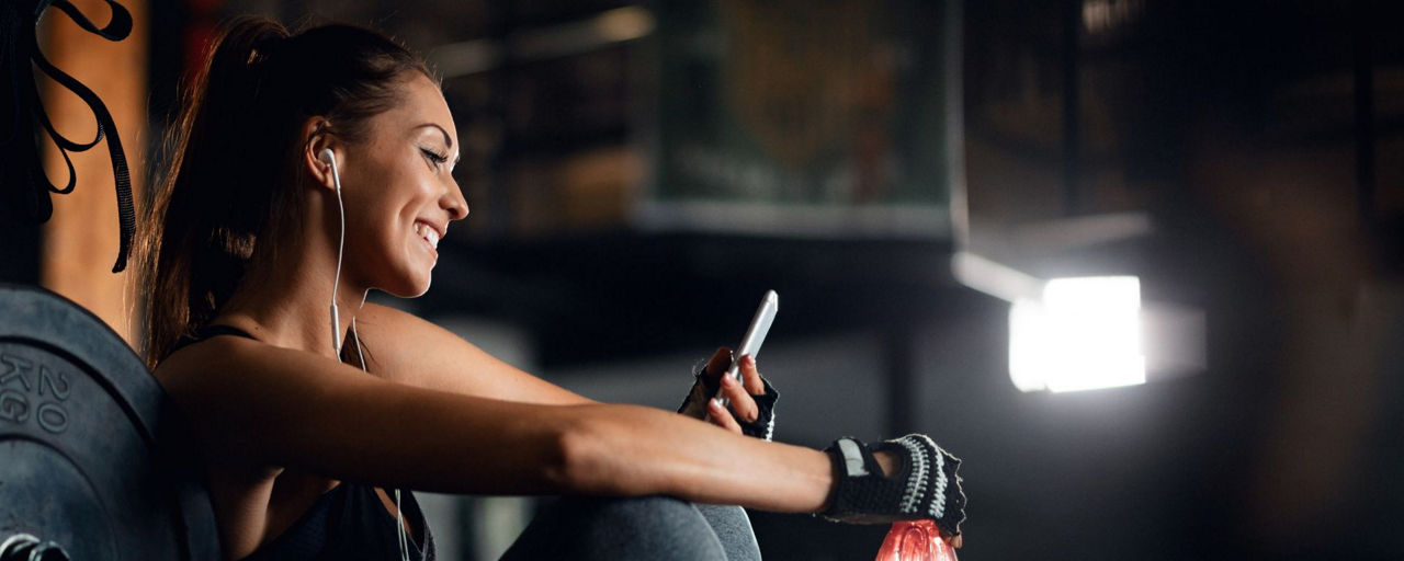 Junge Frau sitzt im Fitnessstudio und schaut auf ihr Handy