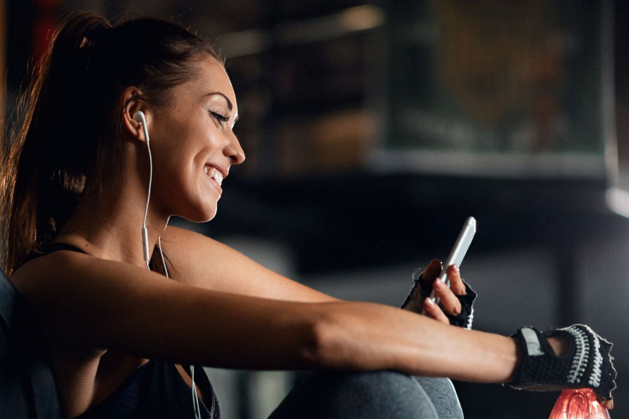 Junge Frau sitzt im Fitnessstudio und schaut auf ihr Handy