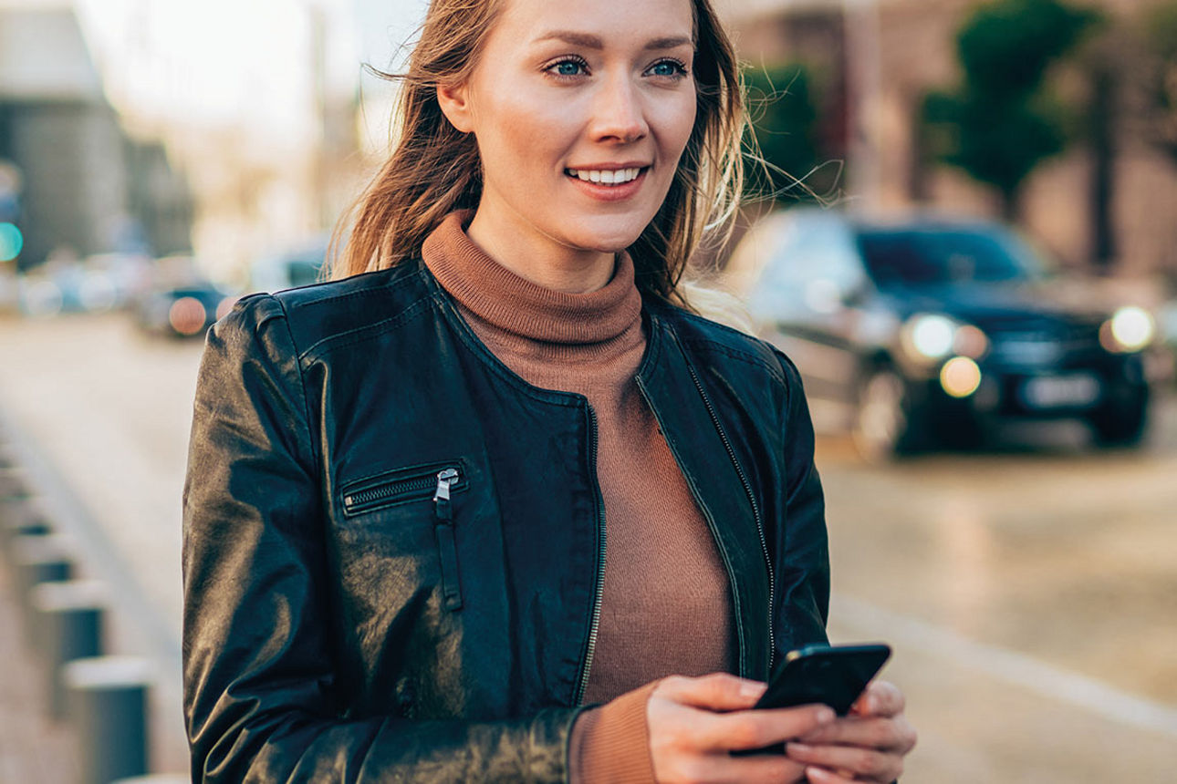 Junge Frau mit Smartphone in der Hand steht auf der Straße und lächelt