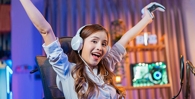 Junges Mädchen jubelt mit Kopfhörern auf dem Kopf und Controller in der Hand