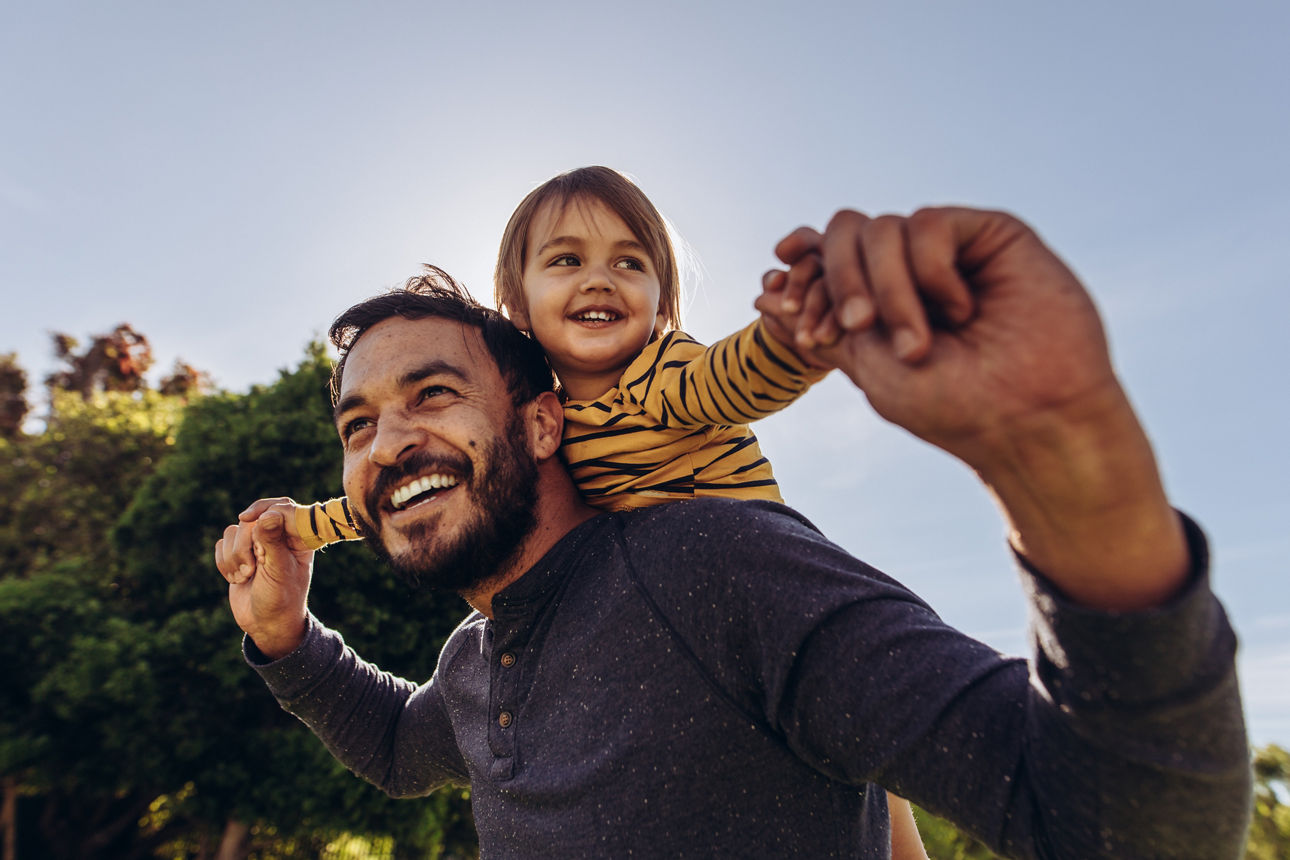 Eine Person, die ein Kind auf den Schultern trägt, beide mit erhobenen Armen