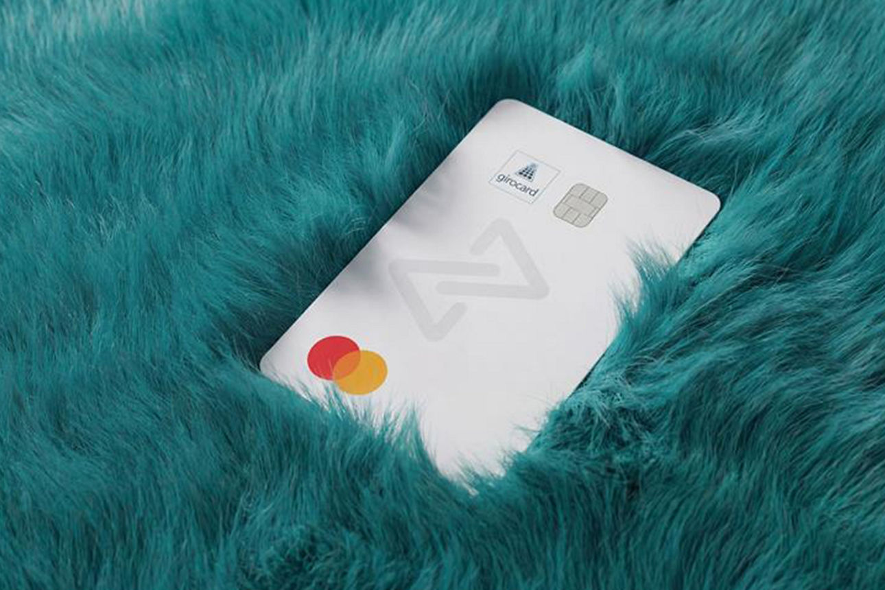 Abbildung zeigt die girocard Debit Mastercard von MEINE BANK in schlichtem, hochwertigen, weißem Design auf petrolfarbenem Fell.