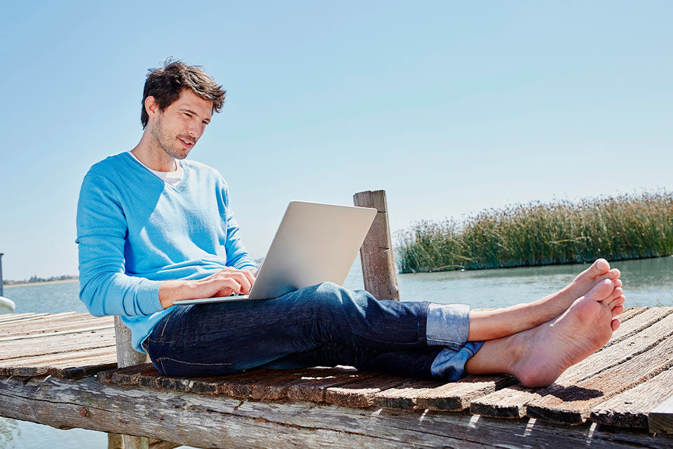 Ein Mann sitzt mit einem Laptop auf dem Schoß auf einem Steg