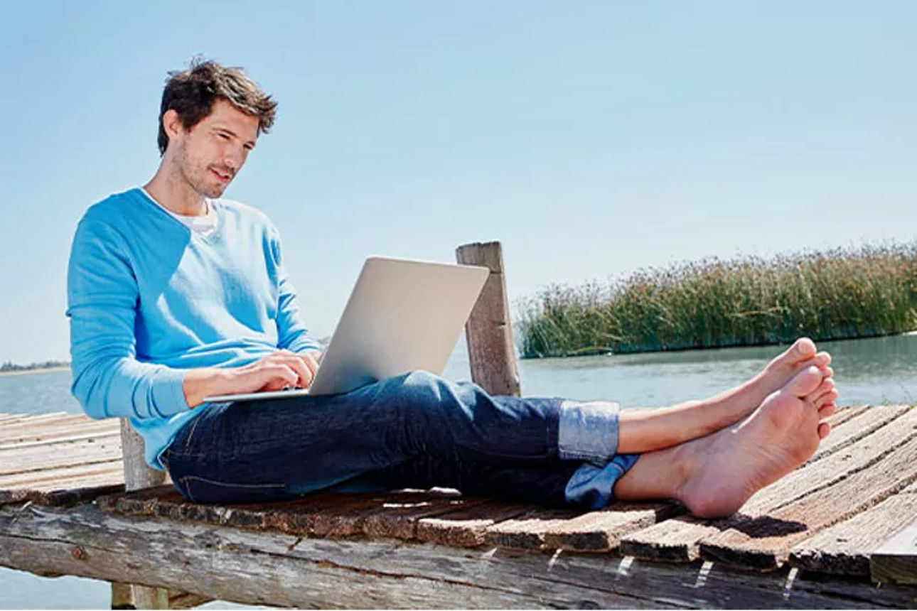 Mann sitzt mit Laptop auf einem Bootssteg