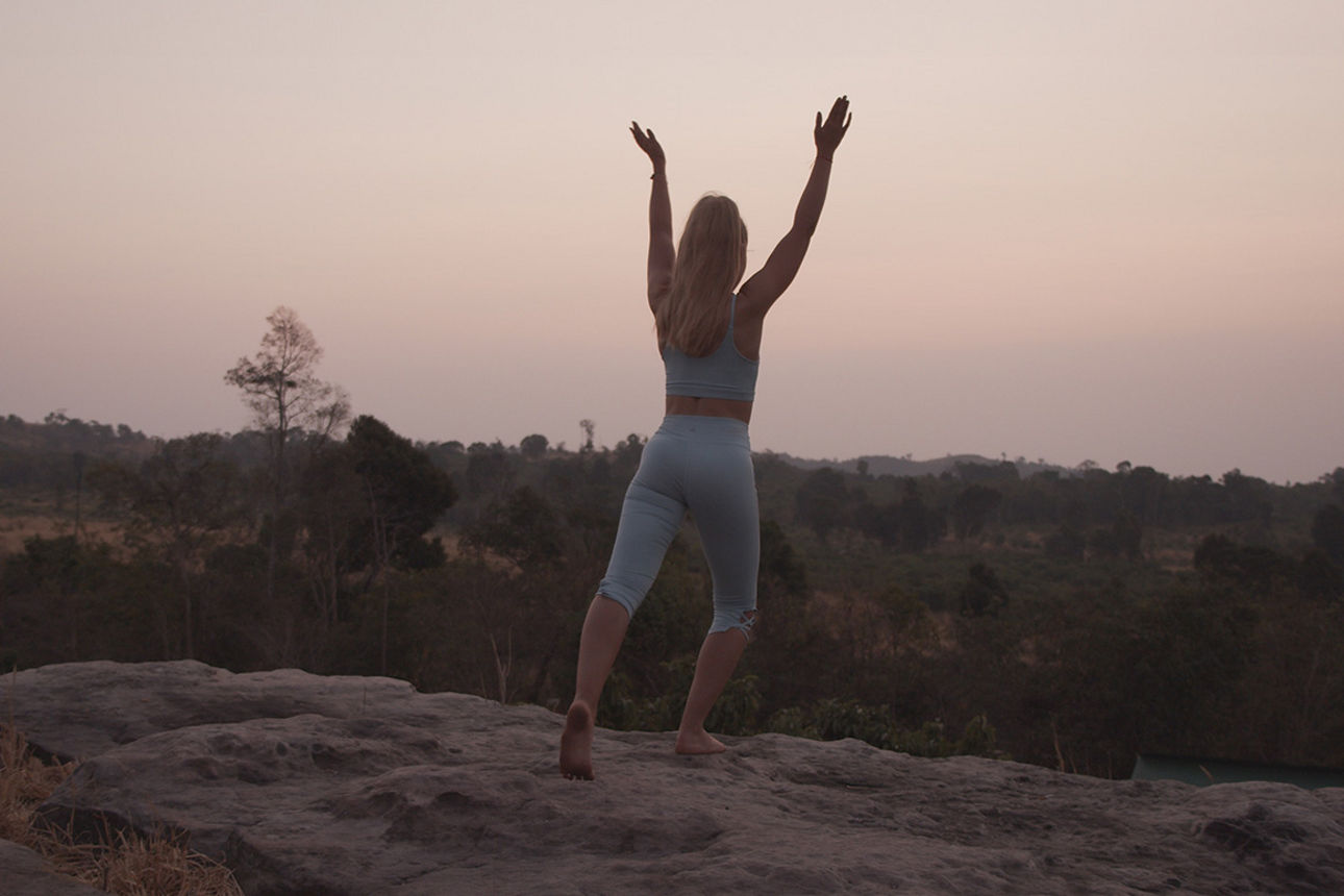 Frau mach in der Dämmerung auf einem Berg Yoga.
