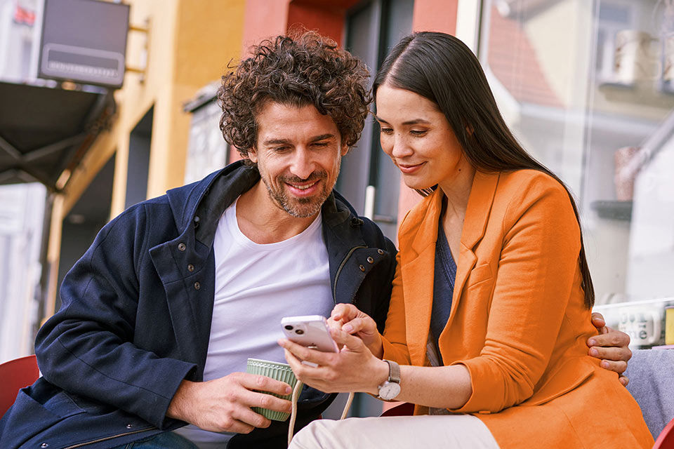 Eine Frau zeigt einem Mann die Vorteile in der MeinPlus Cashback App auf ihrem Handy