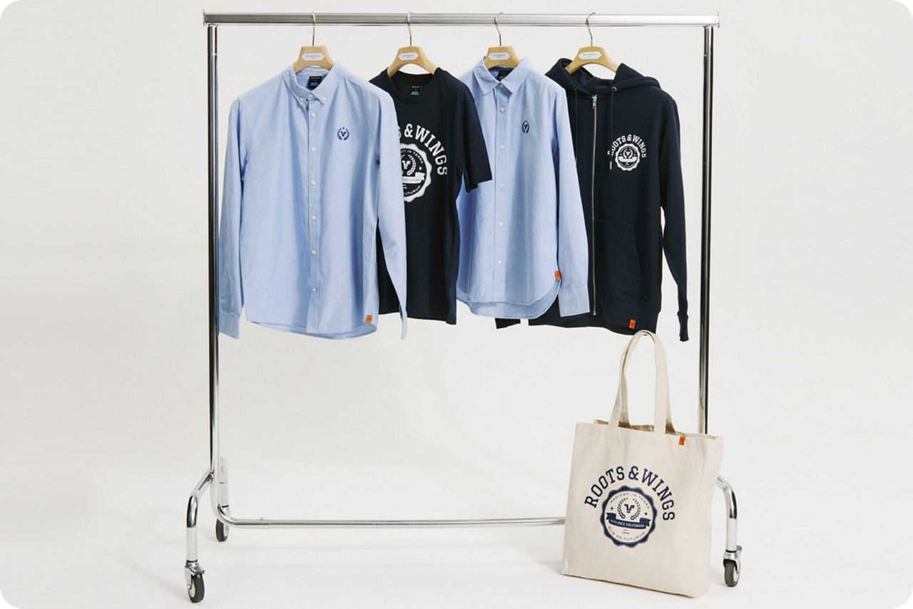 Kleiderständer mit Hemden, T-Shirt, Kapuzenjacke und Stofftasche in Blau- und Naturtönen.