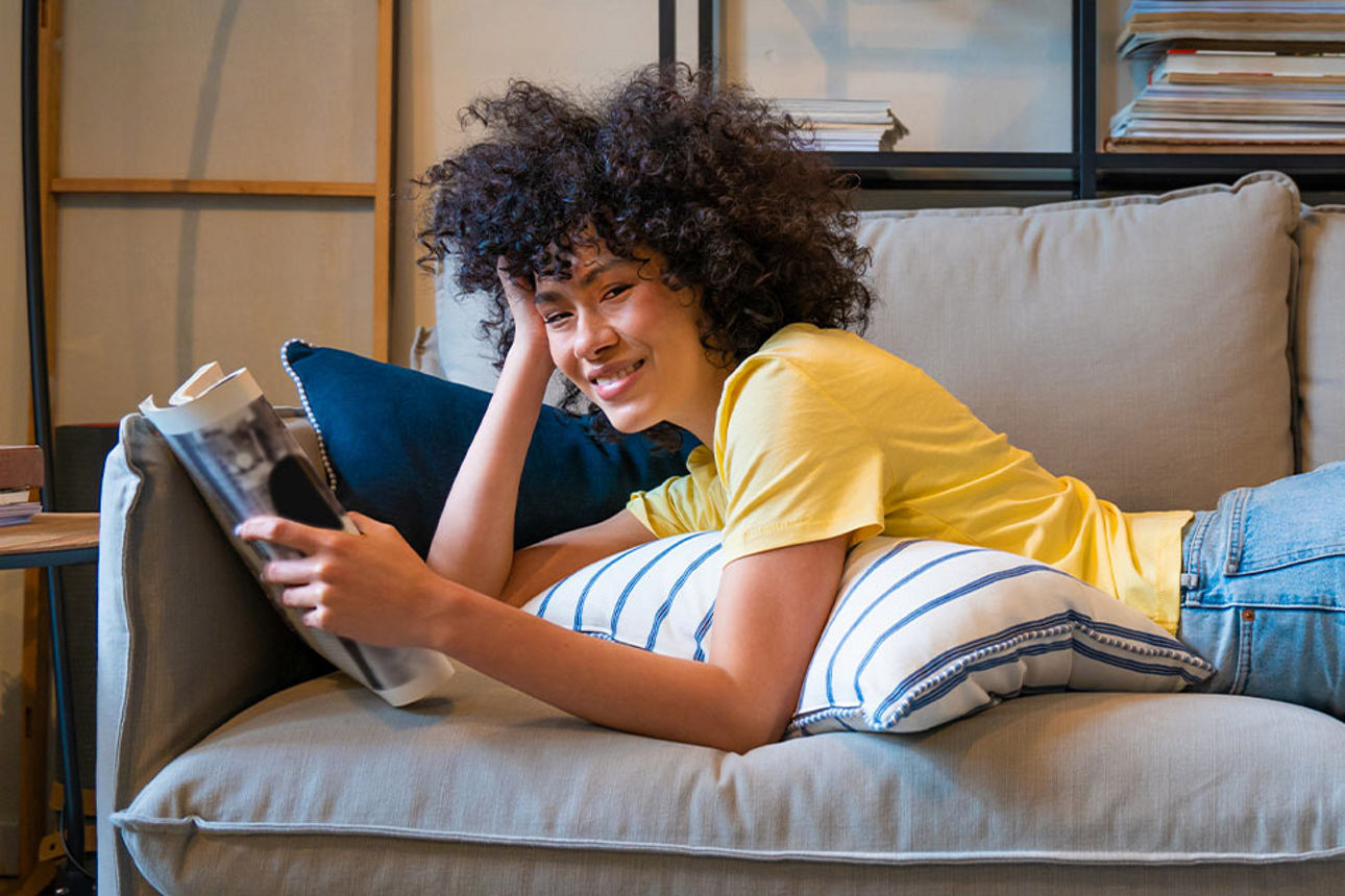 Eine Frau liegt auf der Couch und liest eine Zeitschrift 