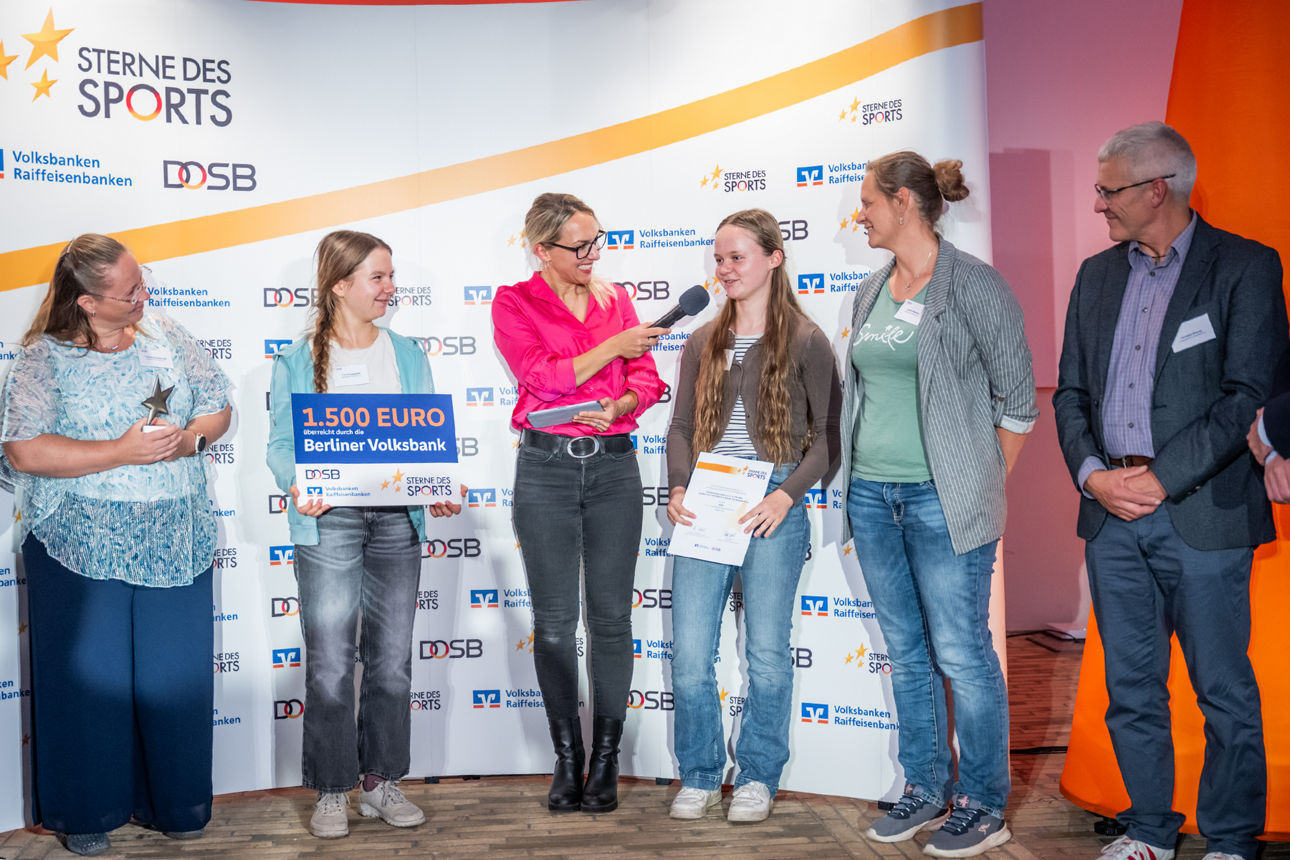 Preisverleihung mit Kindern und Erwachsenen auf einer Bühne, darunter die Übergabe eines Förderschecks.