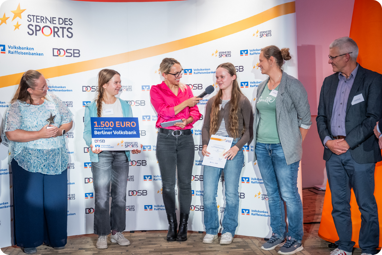 Preisverleihung mit Kindern und Erwachsenen auf einer Bühne, darunter die Übergabe eines Förderschecks.