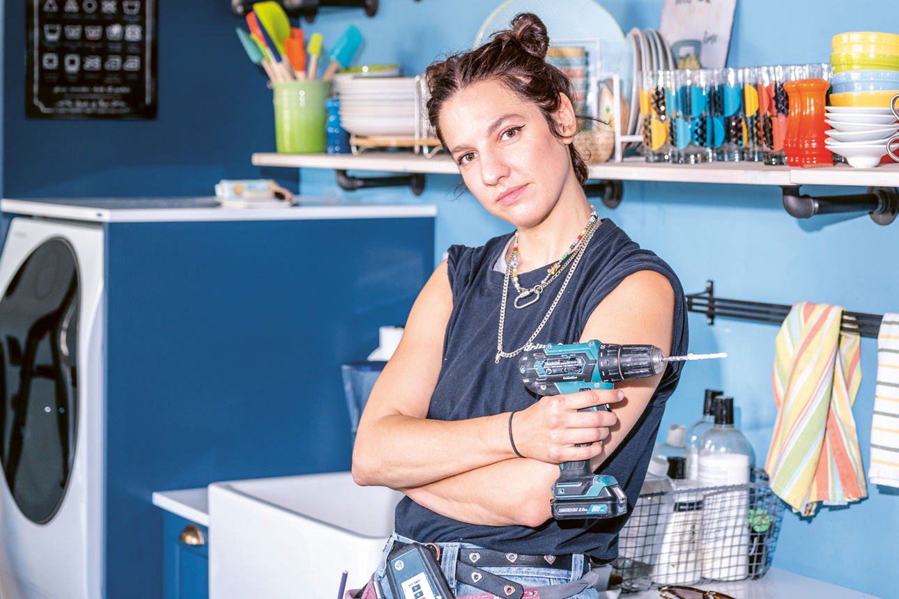 Mit den Driller Queens wird das Handwerk diverser Eine Frau steht mit verschränkten Armen vor einer Spüle und hat einen Akkuschrauber in der Hand