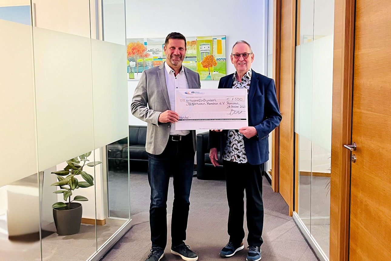 Zwei Männer in einer formellen Umgebung, die einen Scheck in den Händen halten.