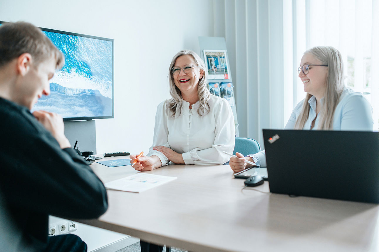 Zwei Frauen sitzen lächelnd mit einem Kunden an einem Beratungstisch.
