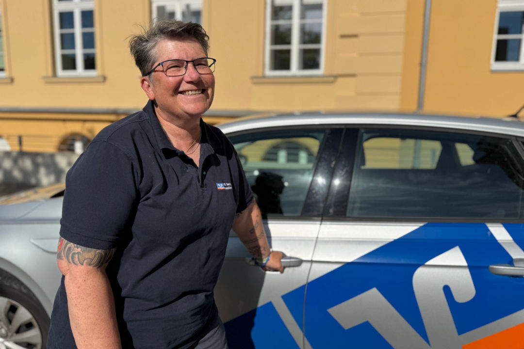 Frau steht vor einem Auto und hält sich am Türgriff fest.