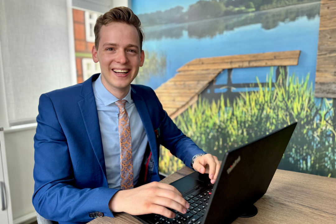 Junger Kundenberater sitzt lächelnd im Beratungsraum am Laptop.