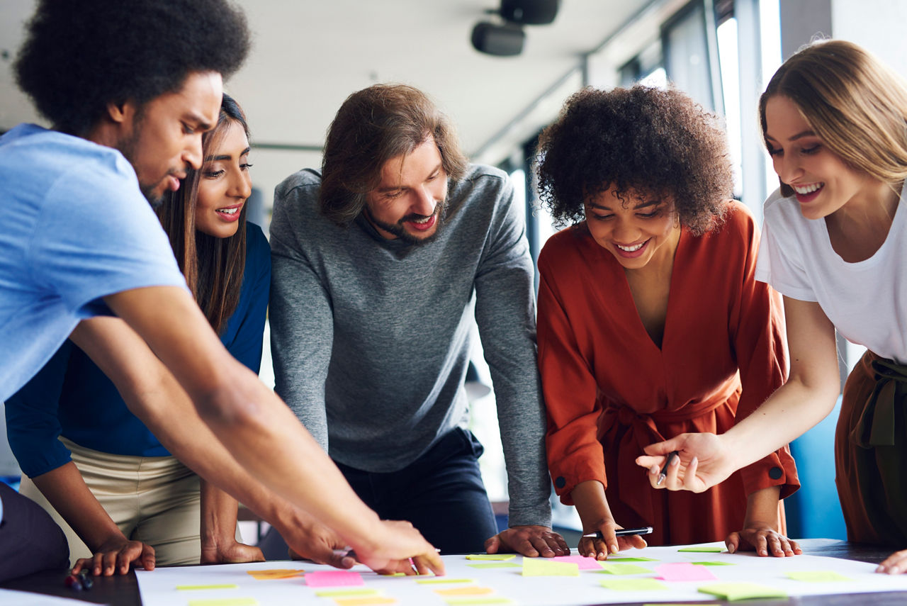 Fünf junge Menschen machen brainstorming im Kreis und notieren ihre Gedanken auf post its