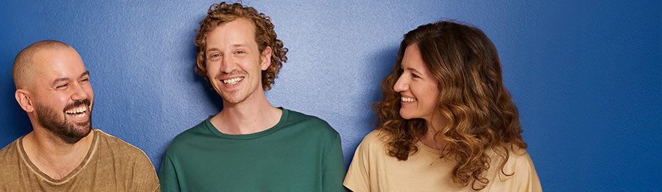 Drei Personen stehen vor einer blauen Wand, lächeln und schauen sich an.