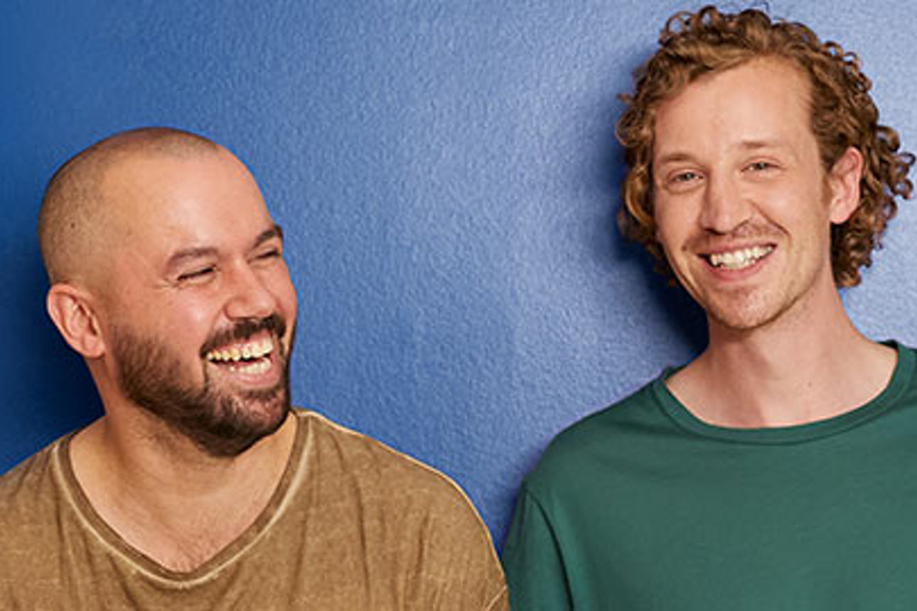 Drei Personen stehen vor einer blauen Wand, lächeln und schauen sich an.