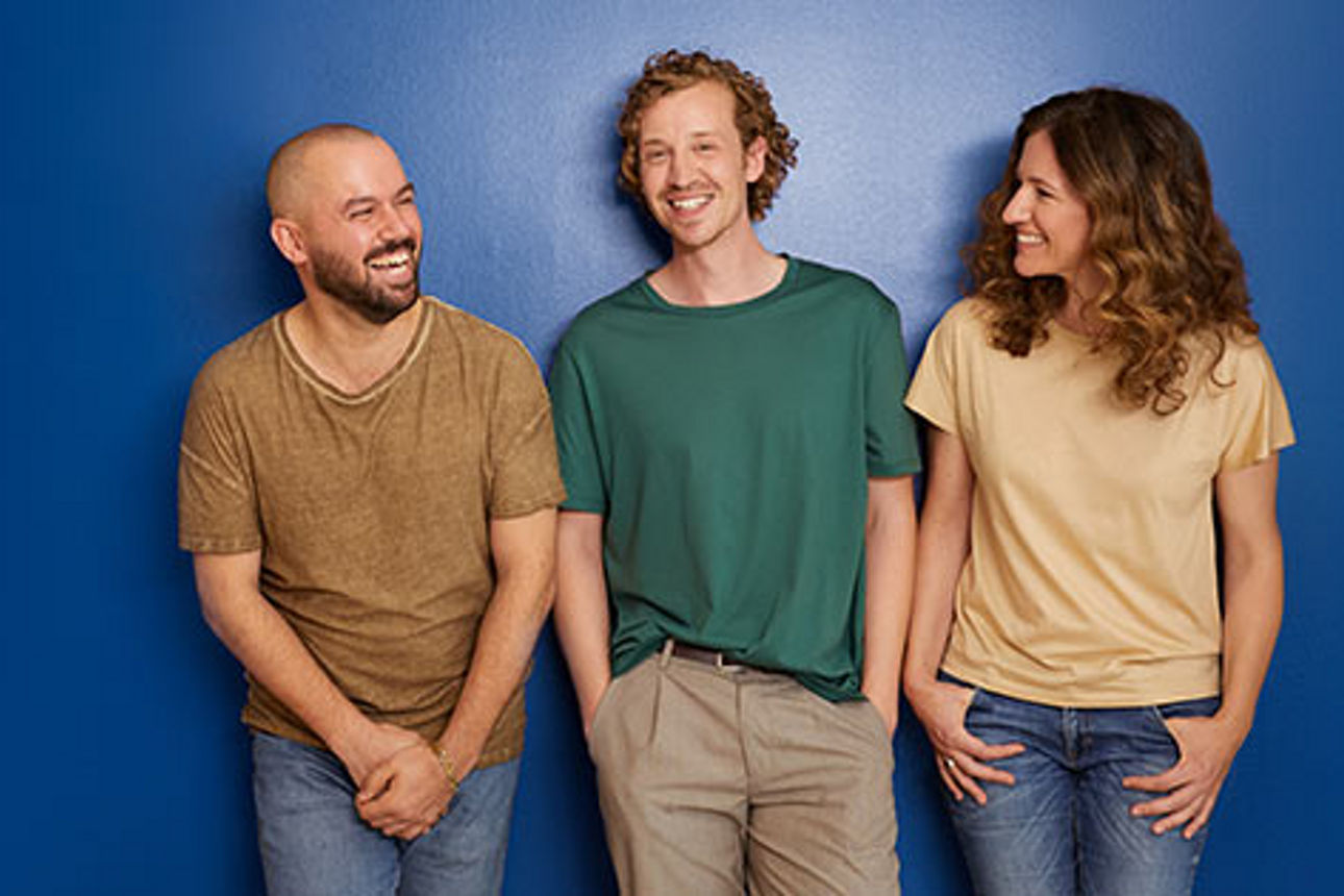 Drei junge Erwachsene stehen vor einer blauen Wand zusammen.