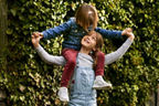 Ein Mädchen trägt ihre kleinere Schwester auf den Schultern, sie lächeln sich an