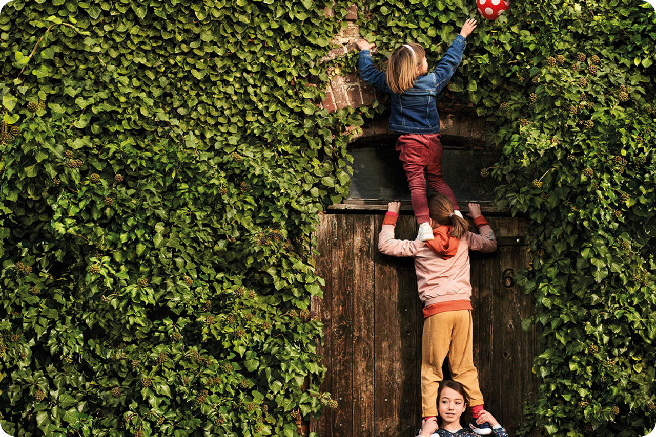 Kinder spielen mit einem Ball vor einer Hecke