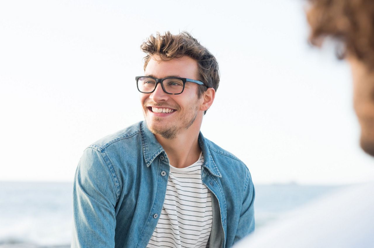 Junger man schaut freundlich lächelnd nach links, im Hintergrund ist das Meer unscharf zu sehen