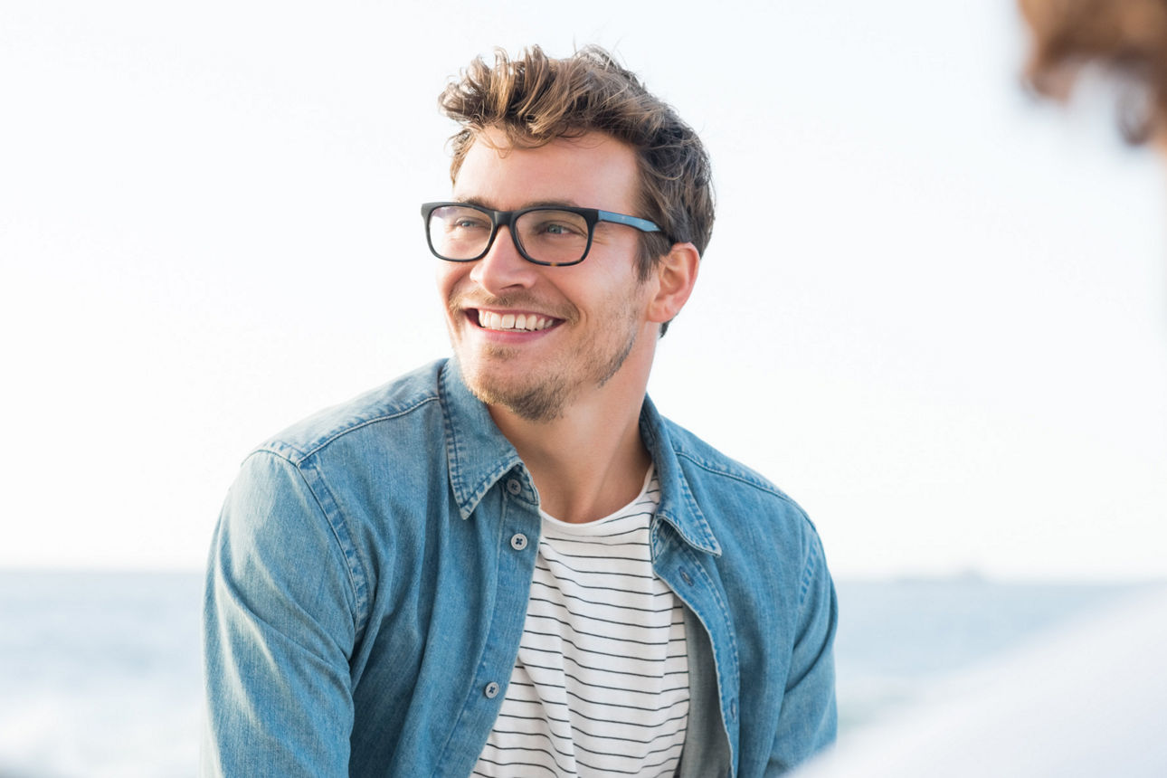 Junger man schaut freundlich lächelnd nach links, im Hintergrund ist das Meer unscharf zu sehen