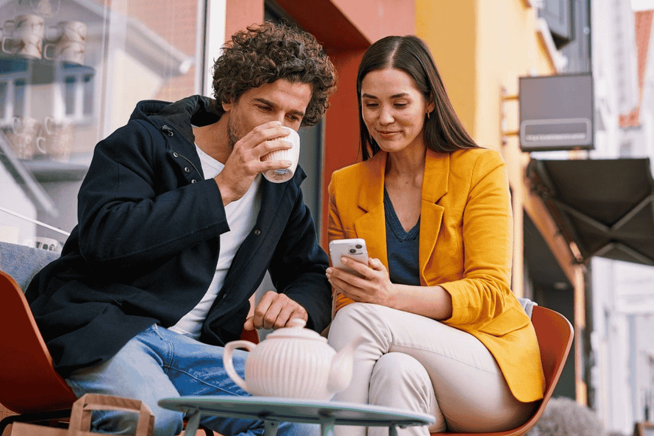 Sitzendes Paar vor einem Cafe mit dem Handy in der Hand