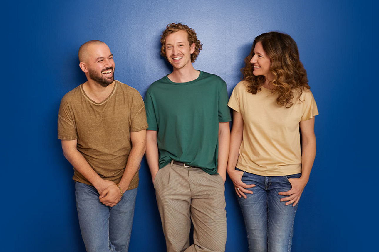 Drei junge fröhliche Personen vor einer blauen Wand