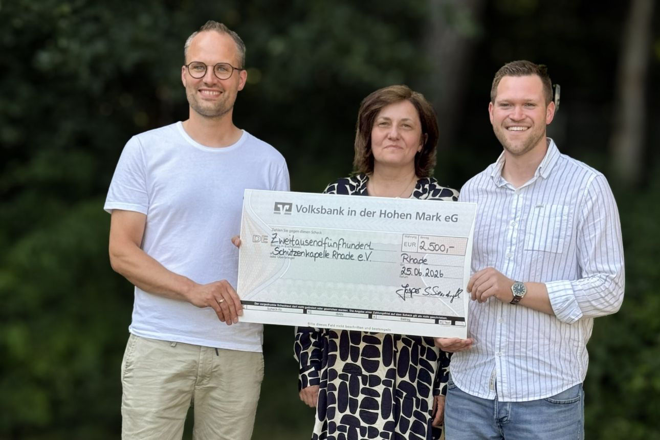 Drei Personen halten gemeinsam einen großen Scheck der Volksbank in der Hohen Mark eG über 2.500 Euro für die Schützenkapelle Rhade e. V. (Datum: 25.06.2026).