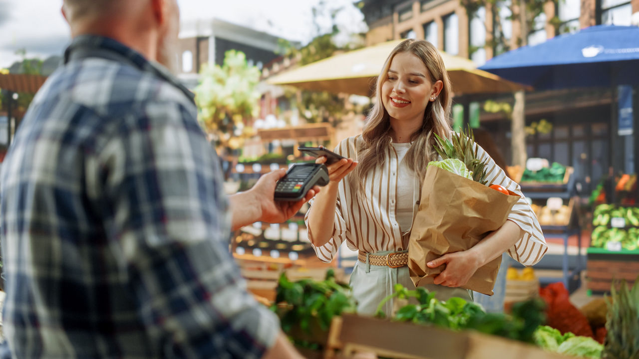 Junge Frau zahlt mobil mit Smartphone auf dem Markt