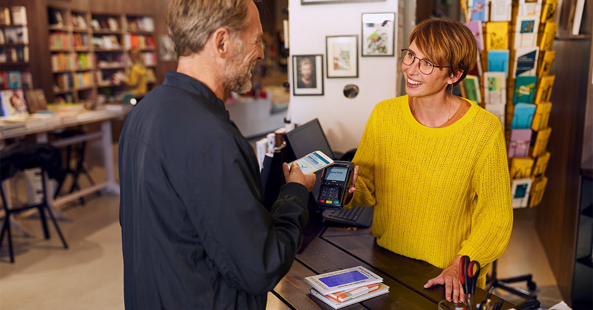 Mann bezahlt in Buchhandlung mit dem Smartphone