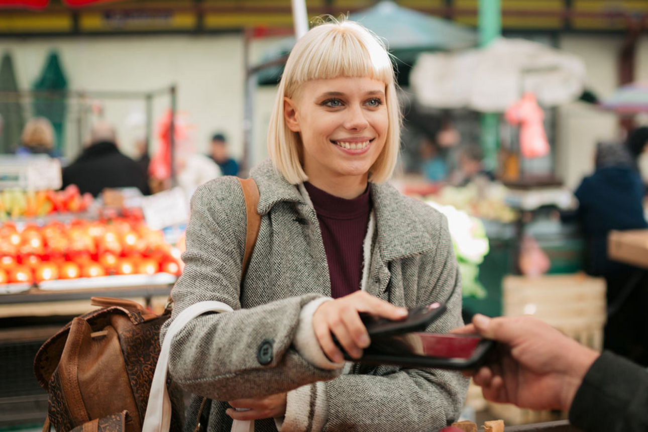 Eine junge Frau zahlt an einem Marktstand mit ihrem Smartphone