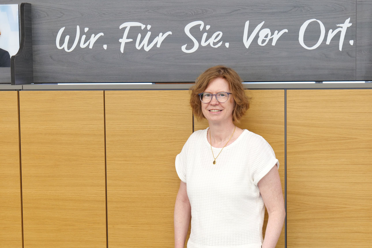 Eine Frau steht vor einem "Wir. Für Sie. Vor Ort." Schild