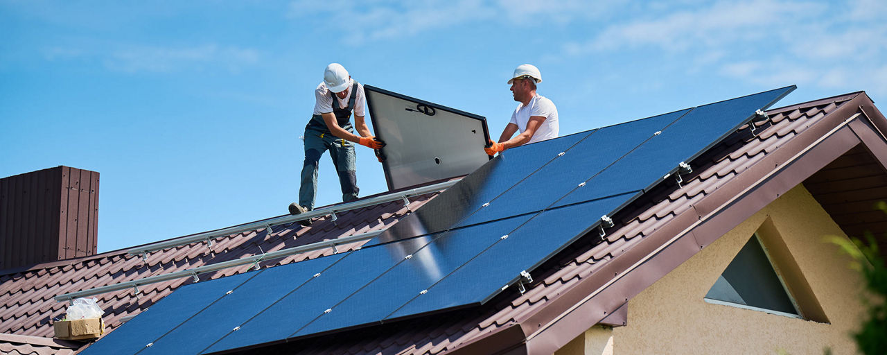 Zwei Handwerker montieren Solarzellen auf einem Hausdach