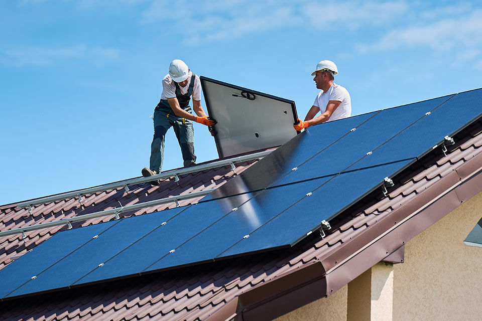 Zwei Bauarbeiter setzen Solarpanele auf einem Hausdach ein