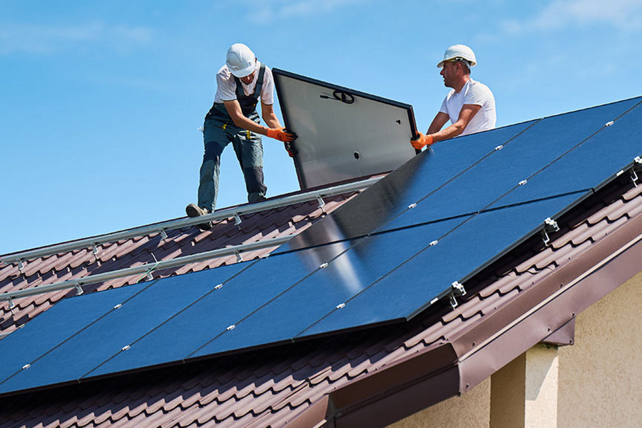 Zwei Bauarbeiter setzen Solarpanele auf einem Hausdach ein