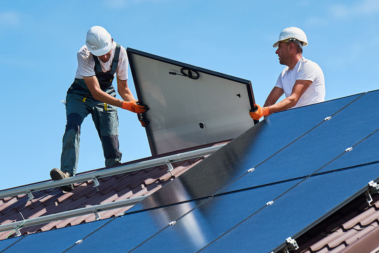 Zwei Handwerker montieren Solarzellen auf einem Hausdach