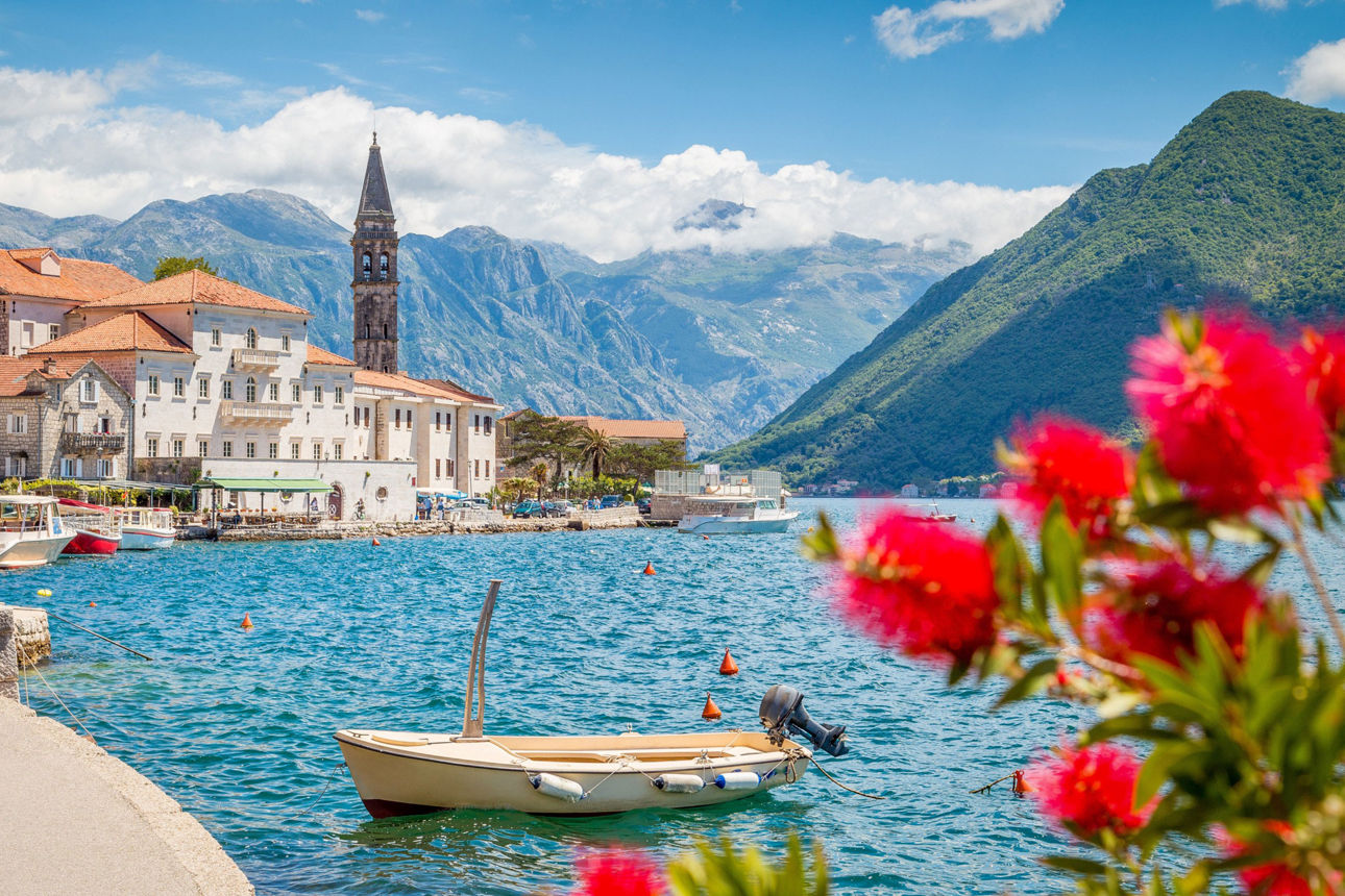 Bucht in Monetnegro mit Kirche und Bergen im Hintergrund und Blumen im Vordergrund